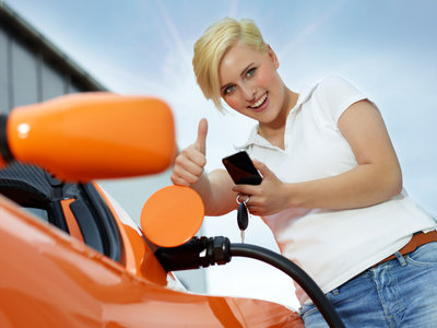 Woman with cellphone loading electrically powered car